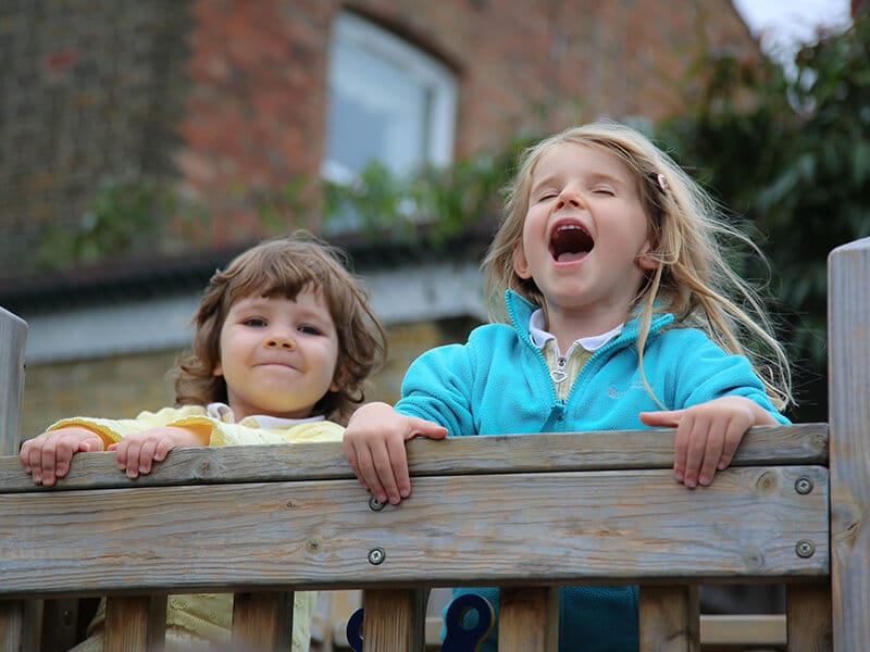 Two happy children enjoying outdoor playtime on a wooden playground at Watford Nursery