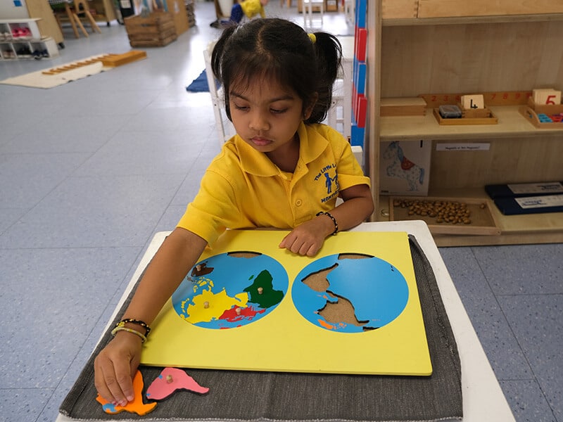 A young student at The Little Learners Montessori focuses on a geography puzzle, learning about continents through hands-on Montessori materials that encourage exploration and independent learning.