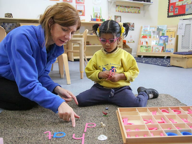 A Montessori teacher at The Little Learners guides a young student through a hands-on language activity, using Montessori materials to explore letter recognition and early word formation, fostering concentration and individualised learning.